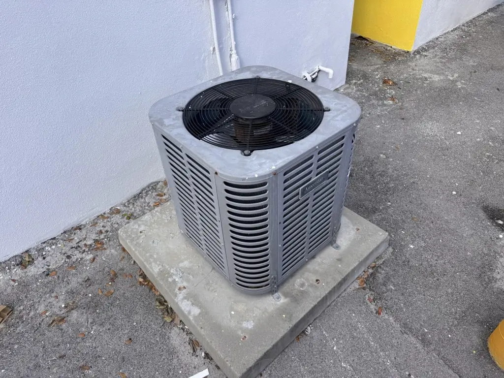 Outdoor air conditioning condenser unit on a concrete pad beside a building wall.