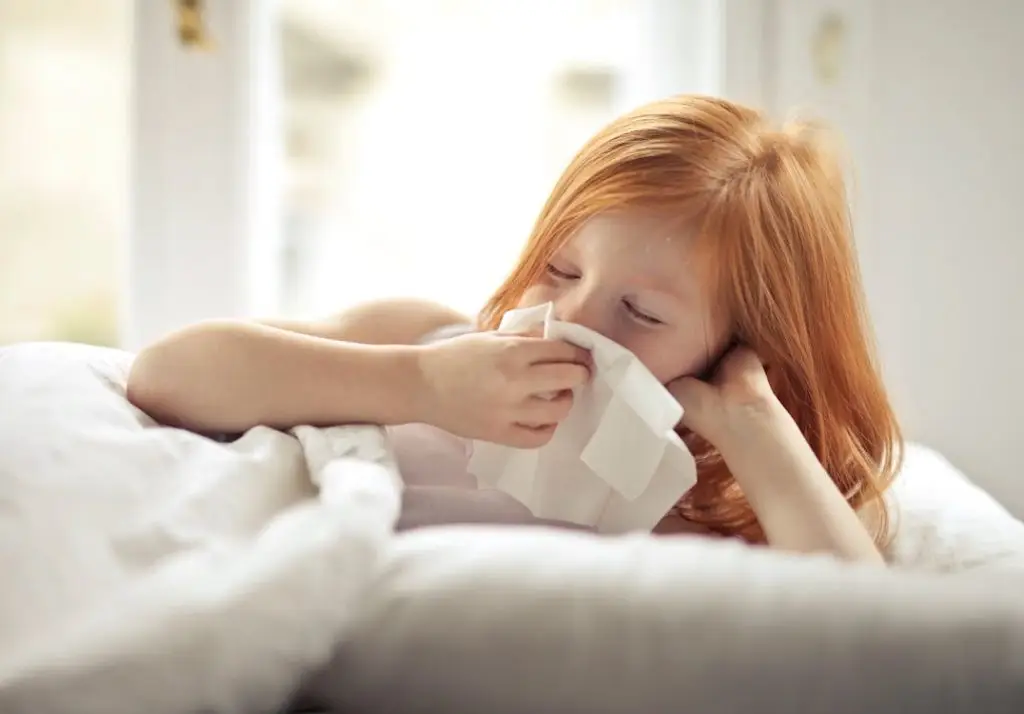 child with allergy symptoms wiping nose with tissue indoors South Florida
